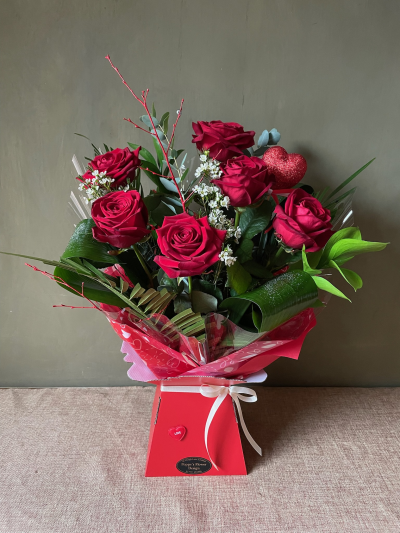 Kissing Booth - Half dozen premium red roses arrange in luscious mixed foliage, completed with a beautiful heart shaped pick.
